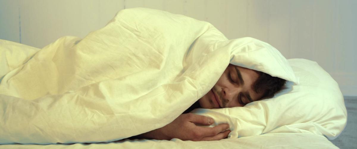 Max liegt, von einer Decke bedeckt, im Bett